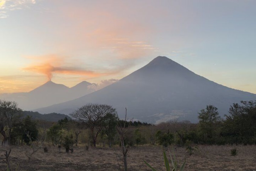 A mountain with a visible plume of smoke, surrounded by sparse vegetation and a clear sky. 2