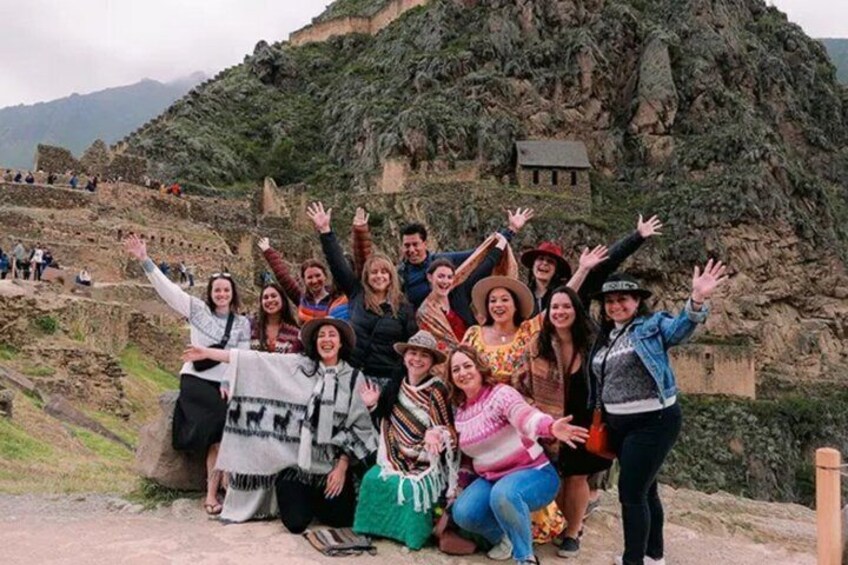A group of people posing in front of an ancient Incan site with stone walls and terraced fields. 2