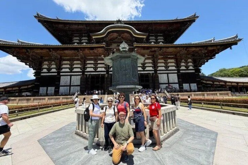 A traditional Japanese building with a large central courtyard and a group of tourists in front. 1