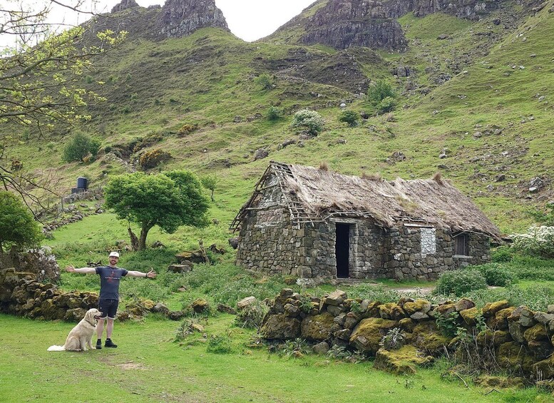 A person with a dog in a rural setting with a stone house and a mountainous backdrop. 5