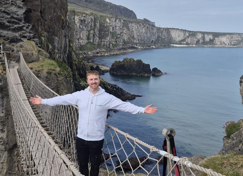 A person standing on a rope bridge with arms outstretched, overlooking a coastal cliff and sea. 1