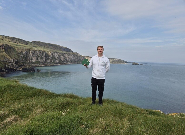 A person standing on a grassy cliff overlooking a calm sea with cliffs in the background. 3