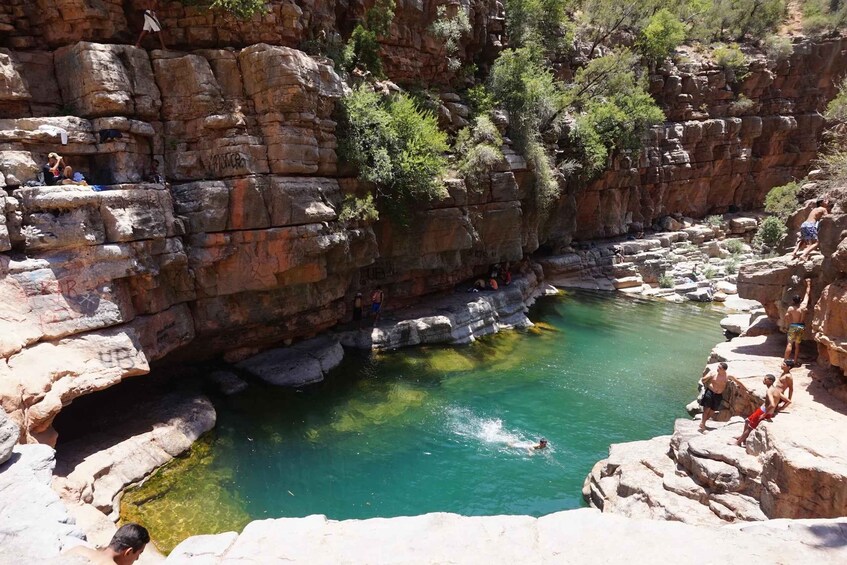 A natural pool surrounded by rocky cliffs with people swimming and standing on the edges. 1