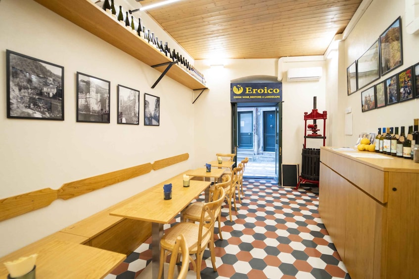 A restaurant interior with hexagonal patterned flooring, wooden tables and chairs, a wine rack, and framed pictures on the walls. 5