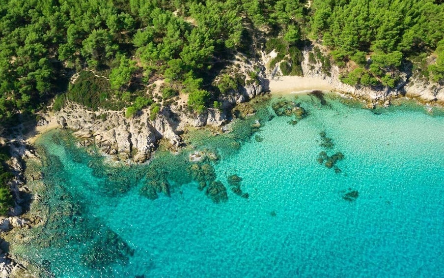 A coastal landscape with clear turquoise waters, rocky outcrops, and dense green forests. 2