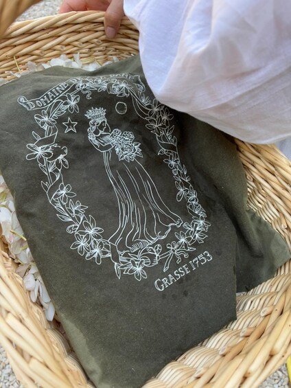 A woven basket containing a fabric with a floral design and the text 'Grasse 1753'. 2