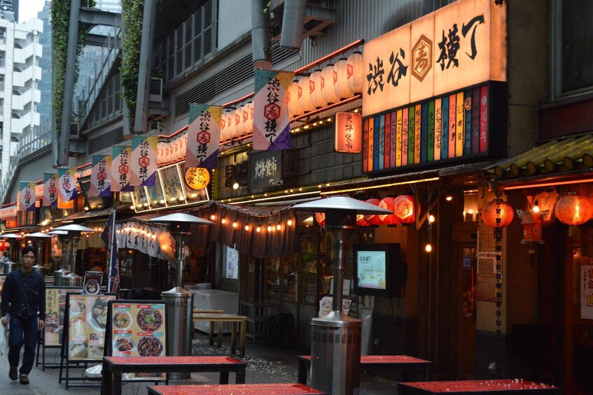A street with traditional Asian lanterns and signage, outdoor seating, and a person walking. 1