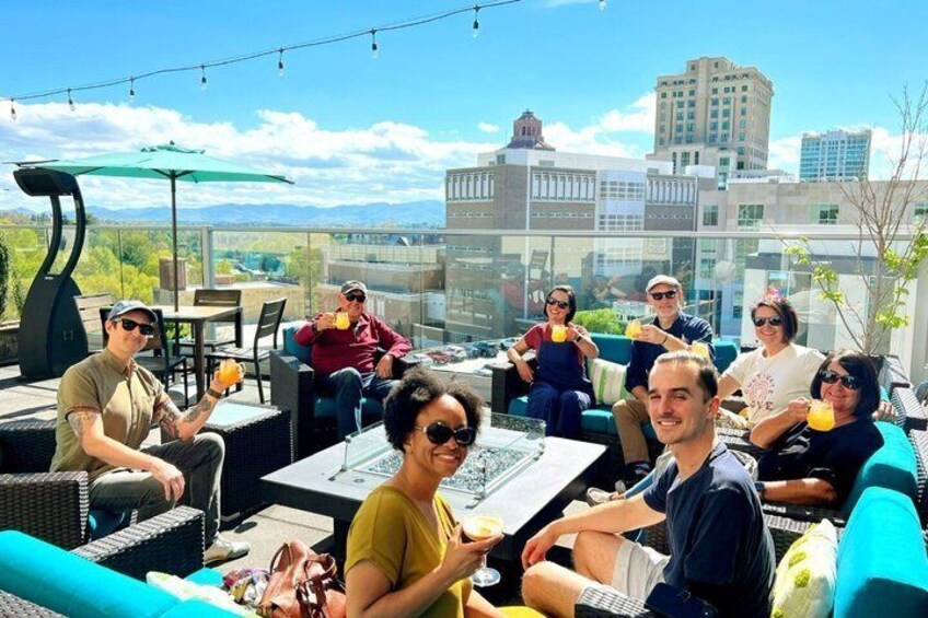 Un gruppo di persone sedute sui mobili da esterno su un tetto con uno skyline sullo sfondo. 1