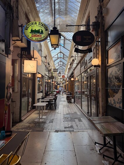 An indoor market with a glass ceiling, shops on either side, and tables and chairs for seating. 3