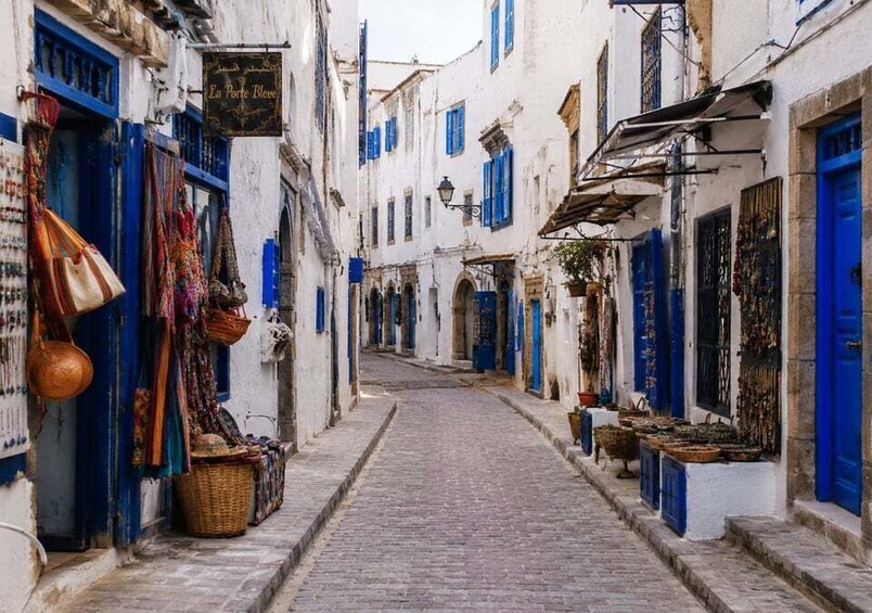 A narrow cobblestone street flanked by white buildings with blue shutters and doors, leading to a distant archway. 3