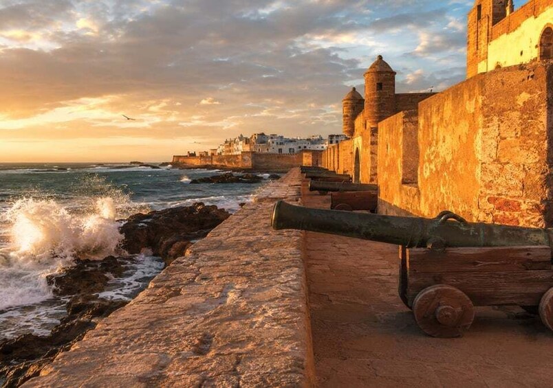 A coastal fortification with cannons, waves crashing against the shore, and a sunset sky. 2