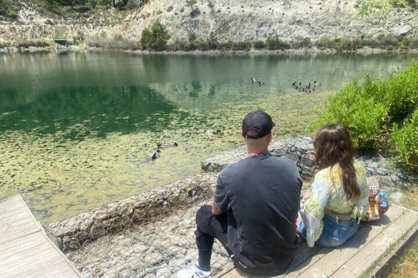 A couple sitting by a lake with ducks swimming in the water. 5