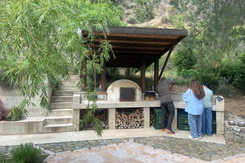 A stone outdoor kitchen with a pizza oven, surrounded by a stone pathway and greenery. 3