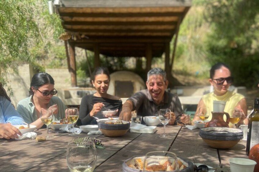 A group of people dining outdoors at a wooden table with food and drinks. 2