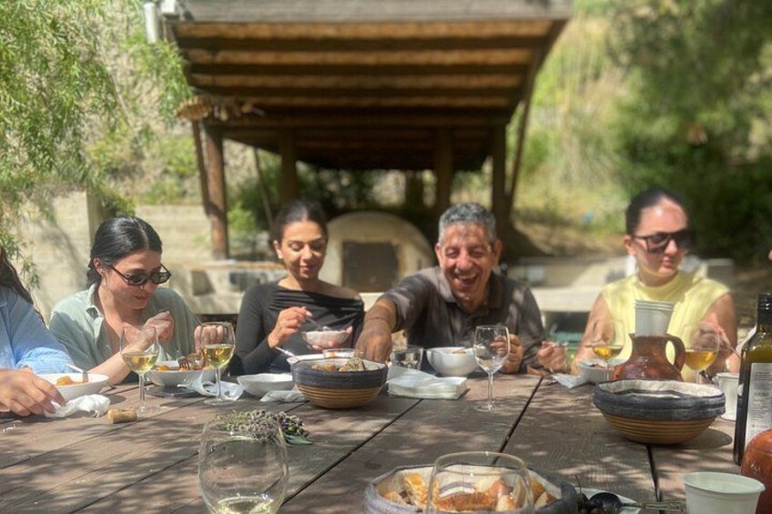 A group of people dining outdoors at a wooden table with various dishes and drinks. 2
