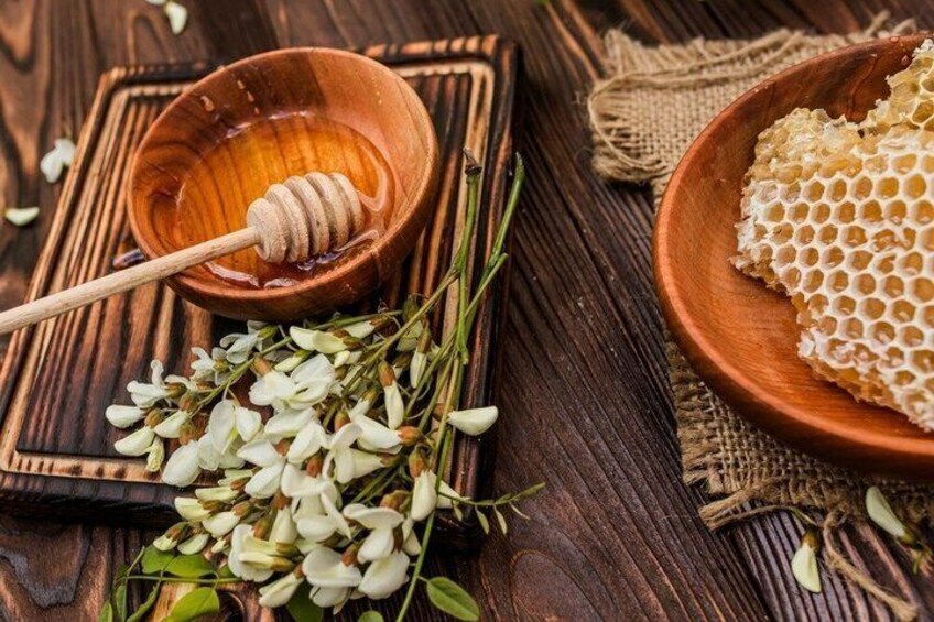 A wooden bowl with honeycomb and a honey dipper on a rustic wooden surface. 1