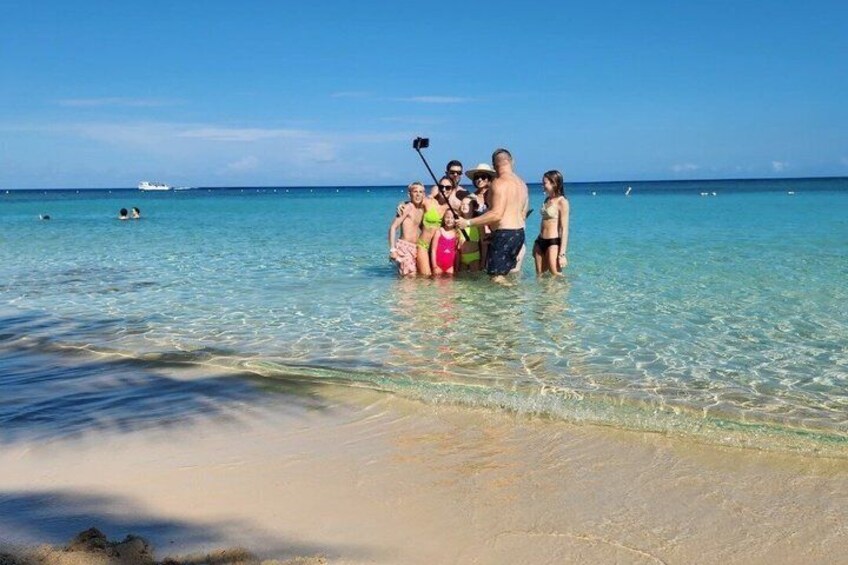 A group of people standing in shallow water at a beach with a clear blue sky and a boat in the distance. 5