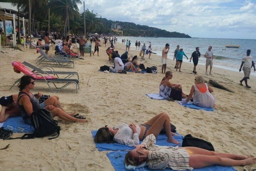 A crowded beach with people sunbathing and walking along the shore. 3