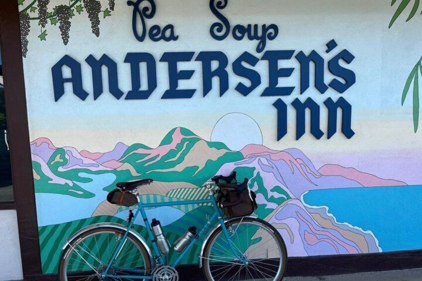 A bicycle parked in front of a building with a mural depicting a landscape and the text 'Pea Soup Andersen's Inn.' 5