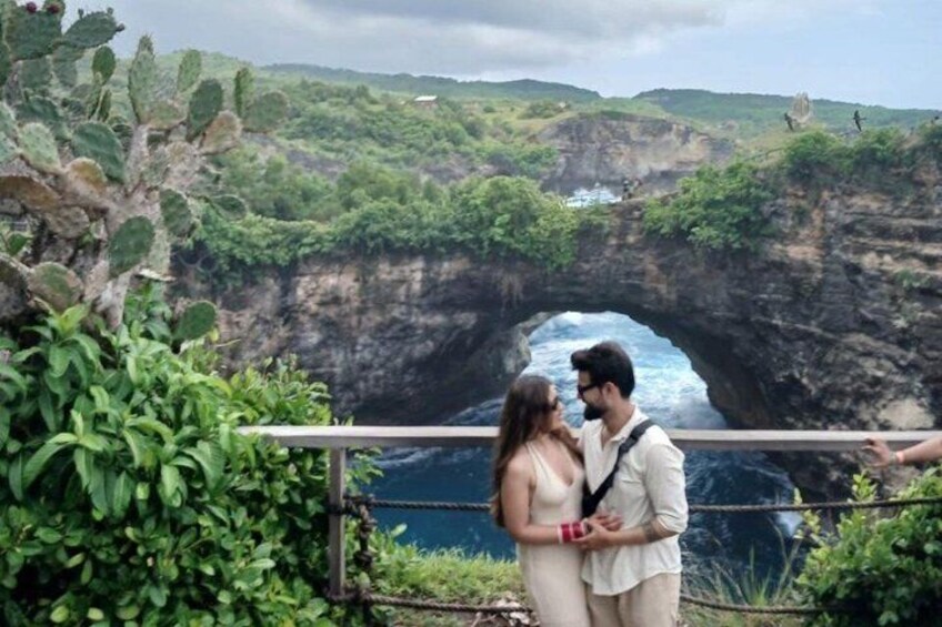 A couple standing by a railing overlooking a natural rock formation with a water body below. 2