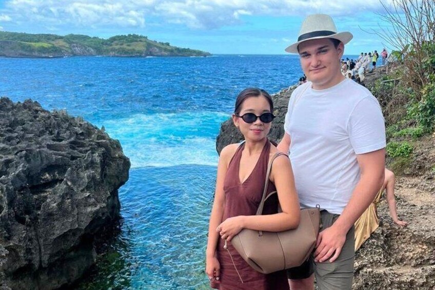 A couple standing on a rocky cliff by the ocean with clear blue water and distant land. 5