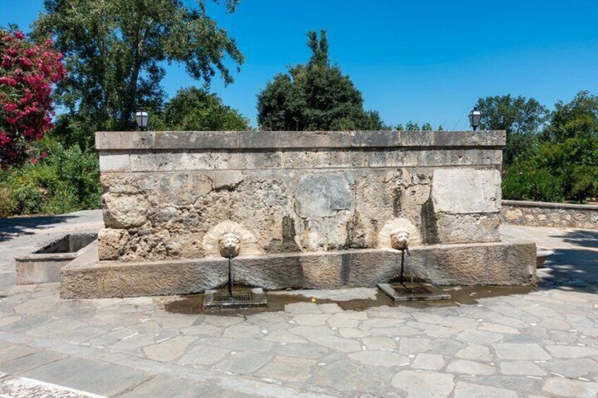 A stone structure with a fountain, surrounded by a stone pavement and greenery. 3