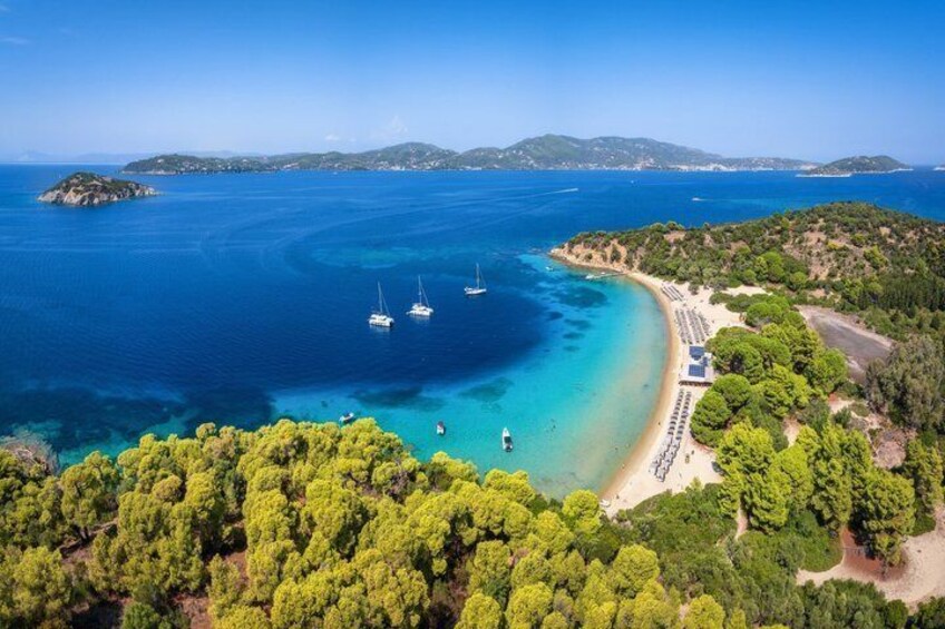 A coastal landscape with clear blue waters, a sandy beach, and a forested area. 1