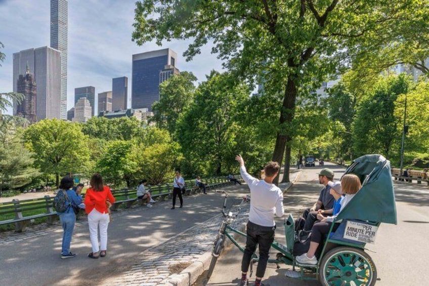 A park with people walking, a green bicycle cart, and a city skyline in the background. 2