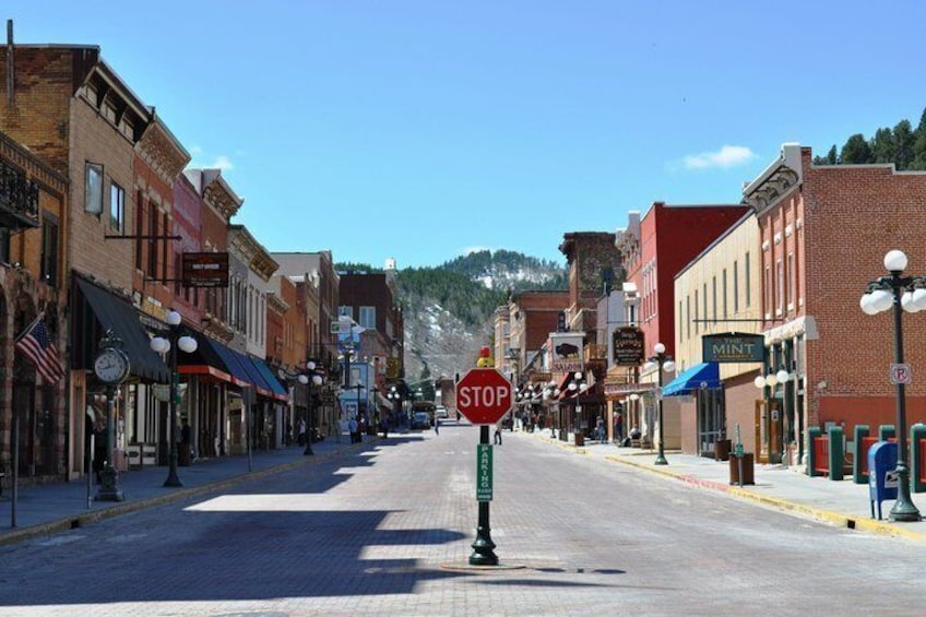 A street lined with brick buildings, a stop sign, and a mountain in the background. 1
