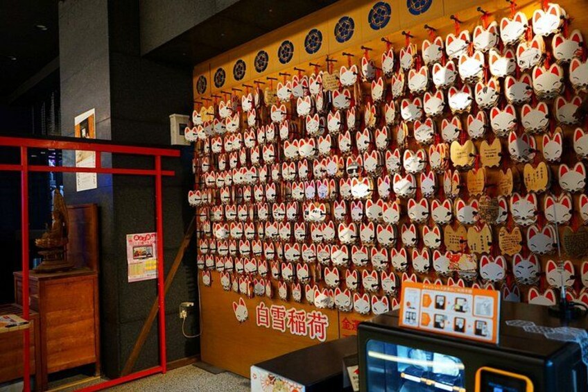 A wall covered with numerous white and red cat-shaped signs, a wooden display case, and a vending machine. 4