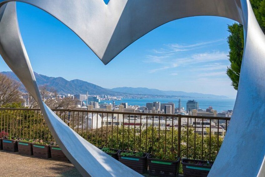 A metal sculpture with a heart shape, overlooking a cityscape with buildings and a distant coastline. 3