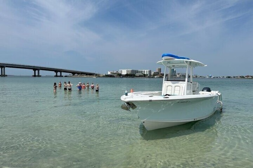 A boat on clear water with a bridge and buildings in the background. 2