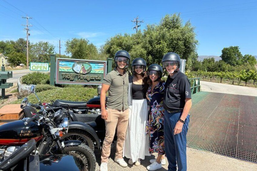 A group of people with helmets, a motorcycle, and a sign that reads 'Wooly Valley.' 1