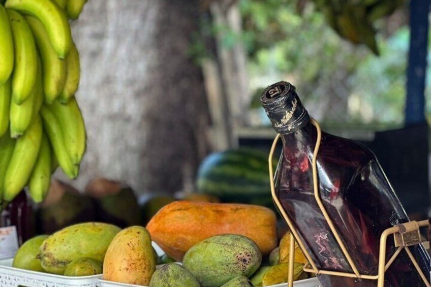 A table with various fruits like bananas, mangoes, and papayas, and a bottle of dark liquid. 2