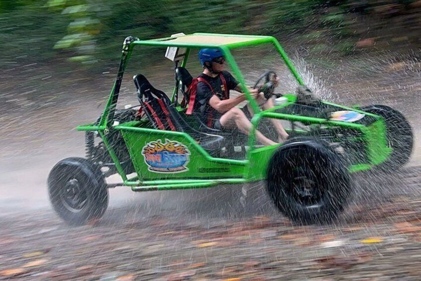 A green off-road vehicle driving through a wet area with water splashing around. 1