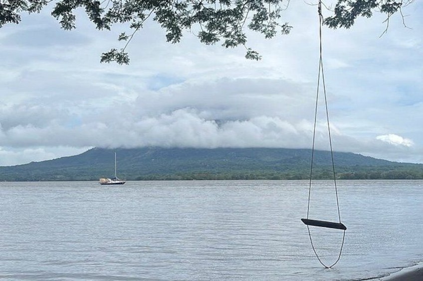 Un lago tranquilo con un velero a lo lejos, una hamaca colgando sobre el agua y una montaña al fondo. 4