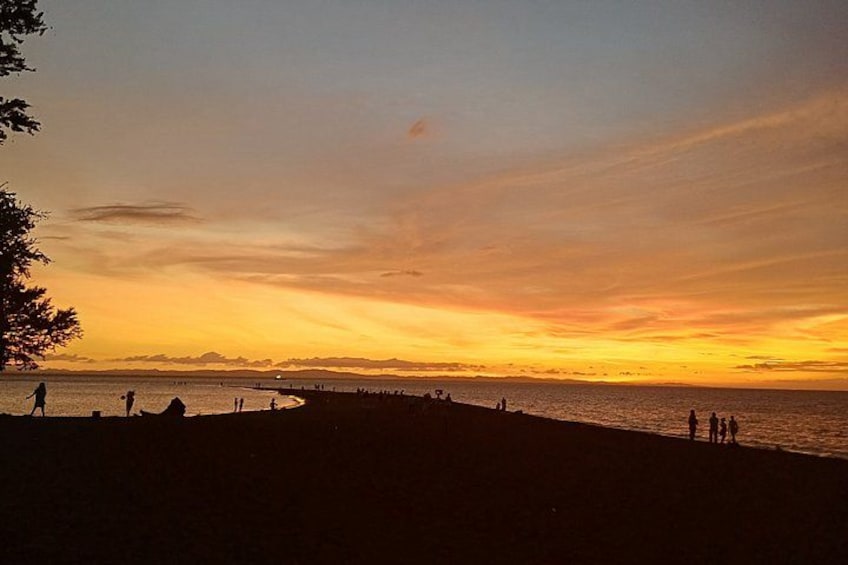 Un atardecer sobre una playa con gente caminando por la orilla. 1