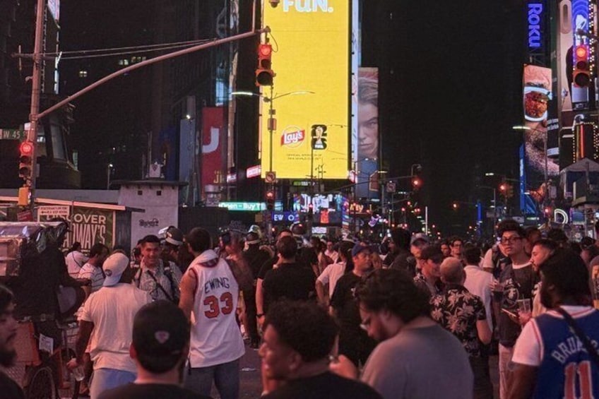 A crowded urban street at night with illuminated billboards and street signs. 4