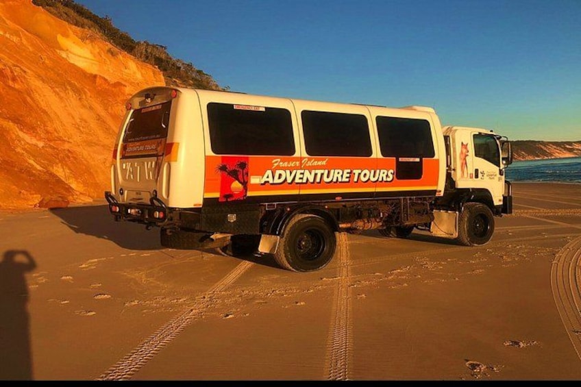 A white van with 'Adventure Tours' written on it parked on a sandy beach. 4