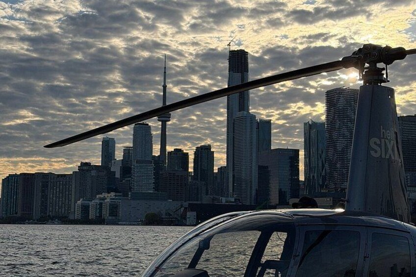 A helicopter with a visible blade, a city skyline with a prominent tower, and a body of water in the foreground. 3