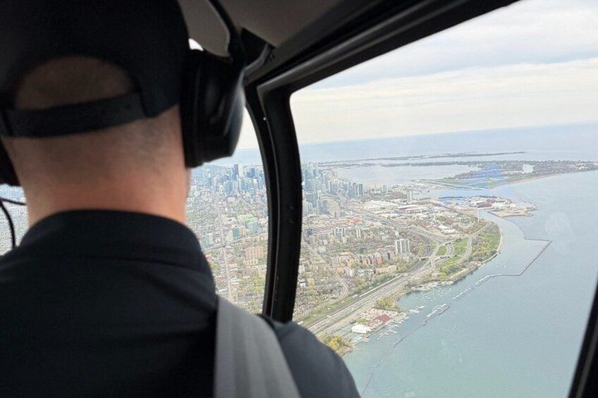A person in a helicopter cockpit with a cityscape and a body of water in the background. 4