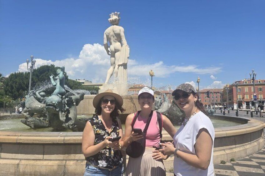 A group of people standing in front of a fountain with statues and a large building in the background. 2