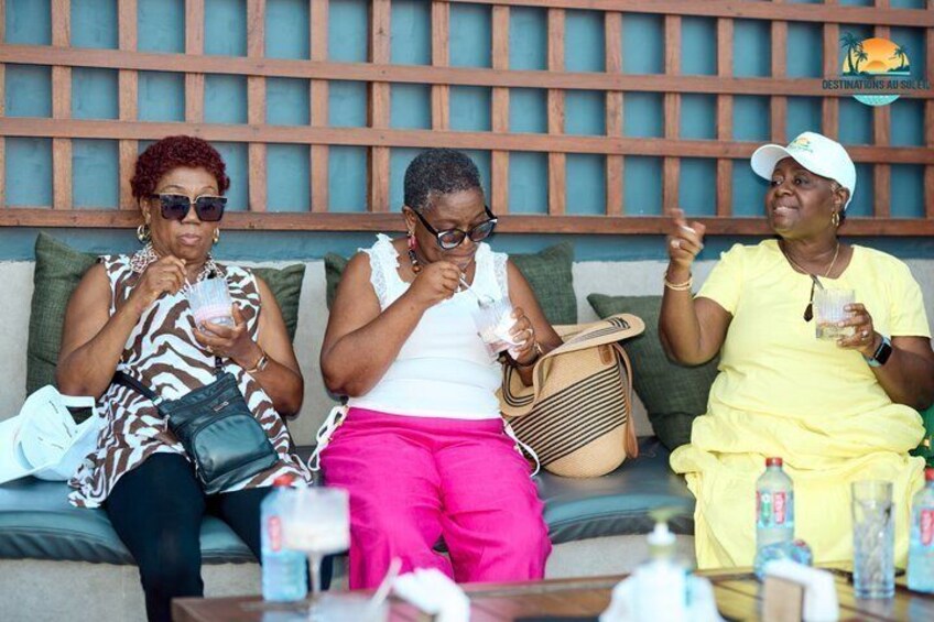 Three people sitting on a sofa with drinks and bags. 3