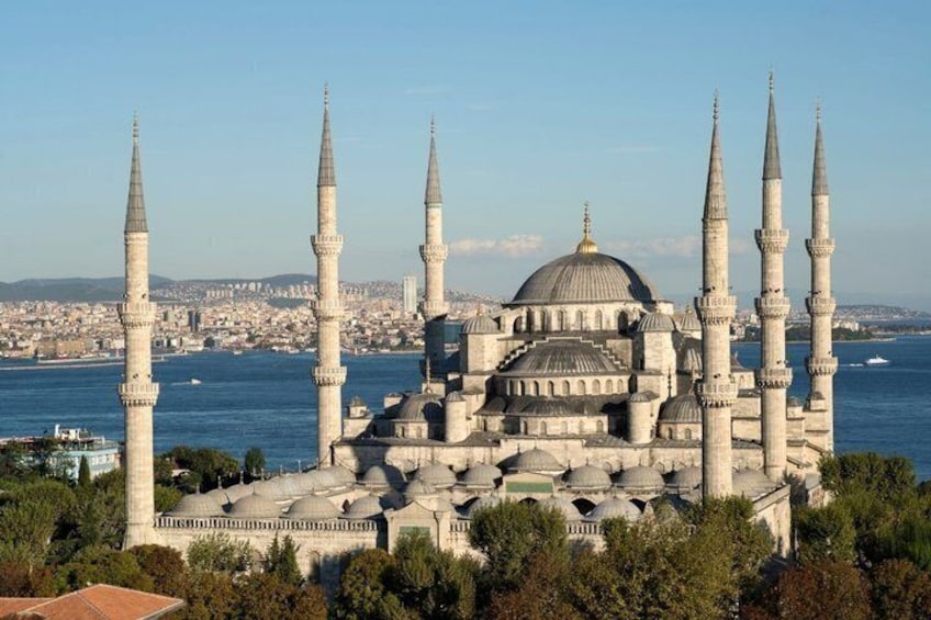 A historic mosque with multiple minarets and a large dome, surrounded by water and a cityscape. 5