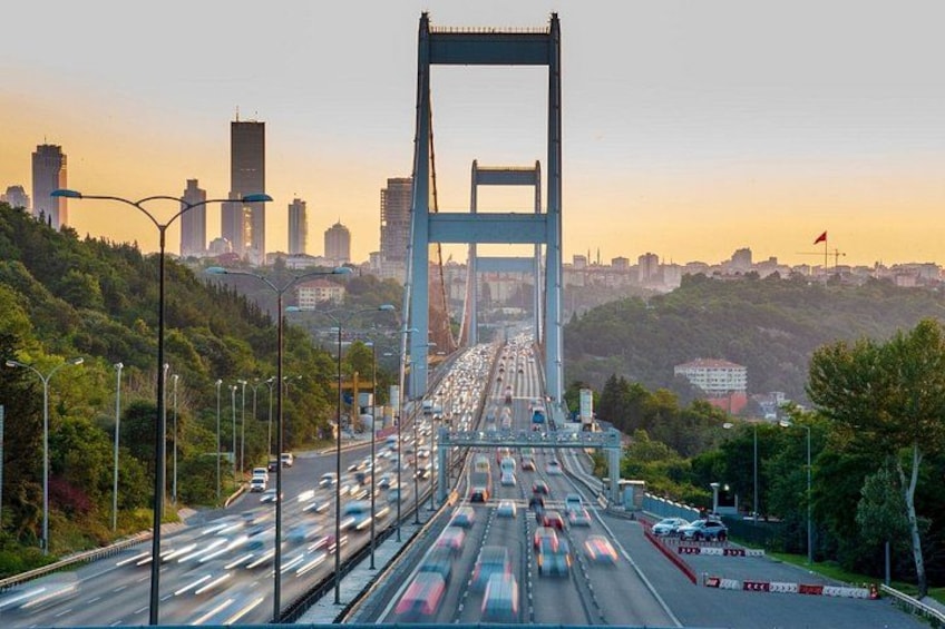 A bridge with multiple lanes of traffic, surrounded by greenery and urban buildings in the background. 1