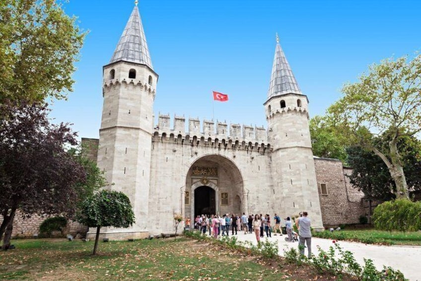 A historic stone gate with two towers, a flag, and a crowd of people. 4