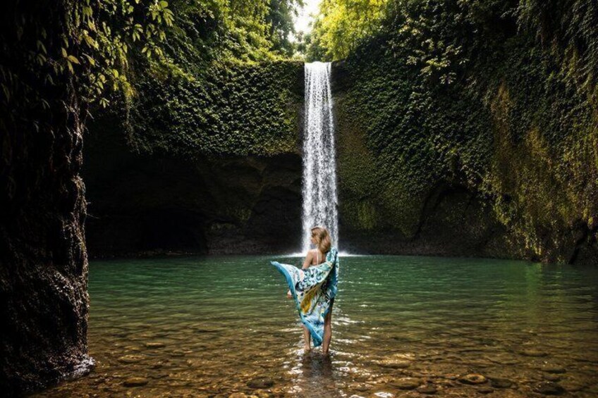A waterfall in a forested area with a person standing in the water. 2