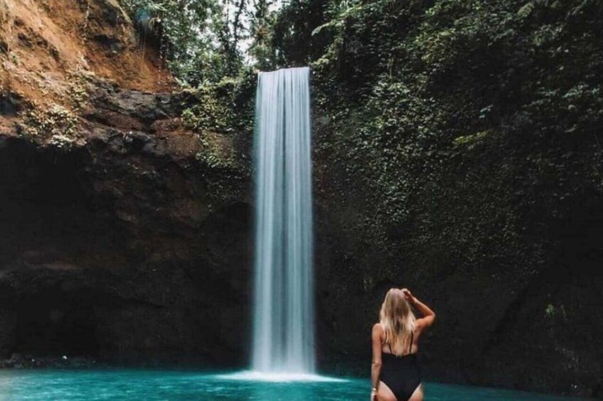 A waterfall, a person in a swimsuit, and a rocky cliff. 2