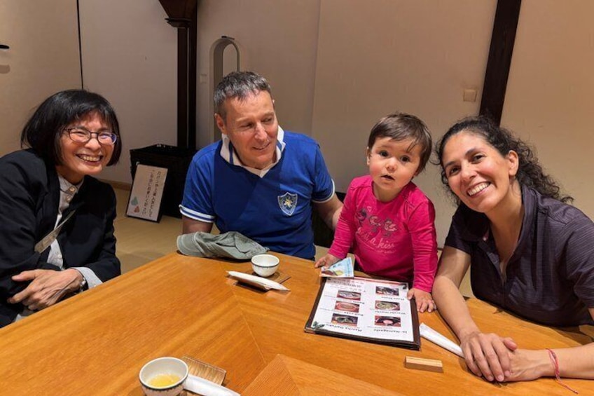 A group of people sitting around a wooden table with a framed photo album and a cup of tea. 4