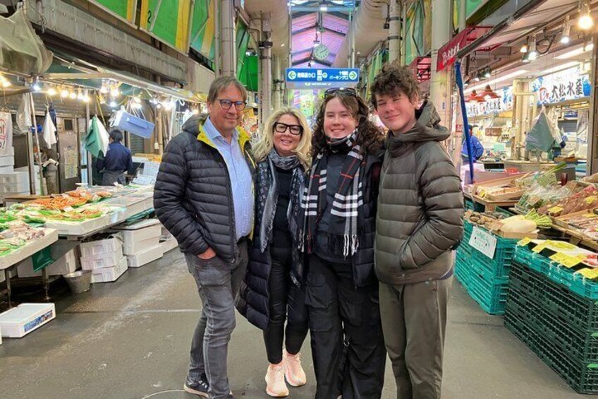 A group of people standing in an indoor market with various food stalls. 1